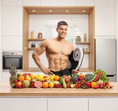 Önünde meyve ve sebzelerle ölçü alan üstsüz genç bir adam beyaz arka planda izole edilmiş. 