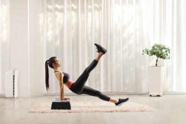Aerobik bir platformda egzersiz yapan ve bir bacağını kaldıran genç bir kadının tam boy profil çekimi. 