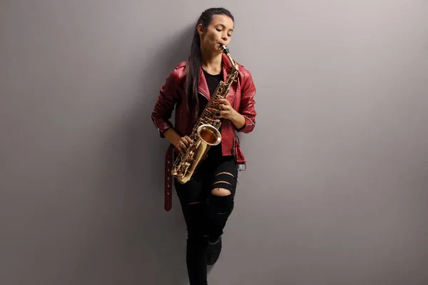 Beautiful woman leaning on a gray wall and playing sax