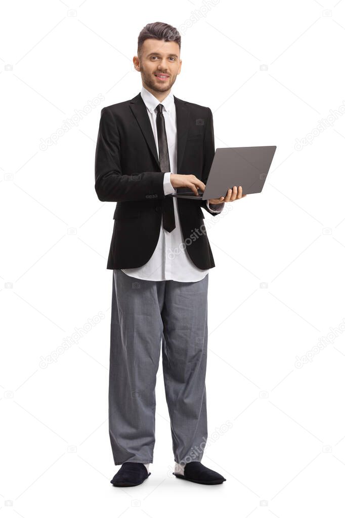 Full length portrait of a businessman in a suit and pajamas standing and working on a laptop isolated on white background