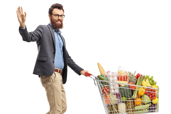 一个留着胡子的男人 拿着一辆装有食品的购物车走着 挥动着与白色背景隔离的手 — 图库照片