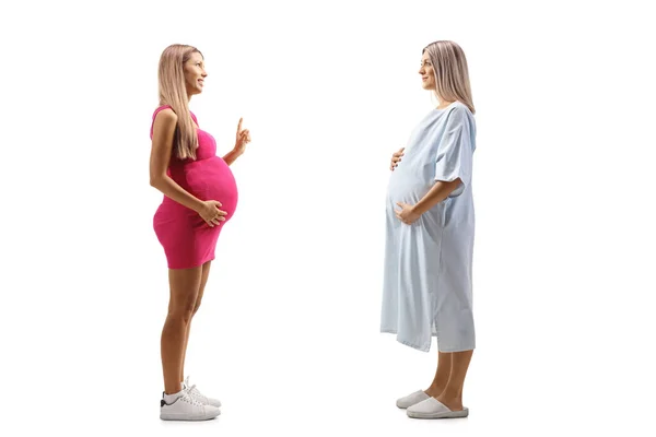 フル丈プロファイルショットの妊娠中の女性でザ 患者のガウンとA妊娠中の女性でピンクのドレス話隔離された白い背景 — ストック写真