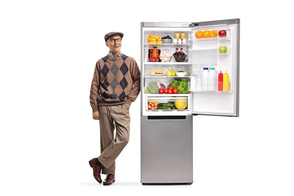 陽気な高齢者の男にもたれてオープン冷蔵庫の上に健康的な食べ物の完全な白い背景に隔離 — ストック写真