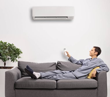 Uzaktan kumandalı pijamalı genç adam evde klima takıyor.