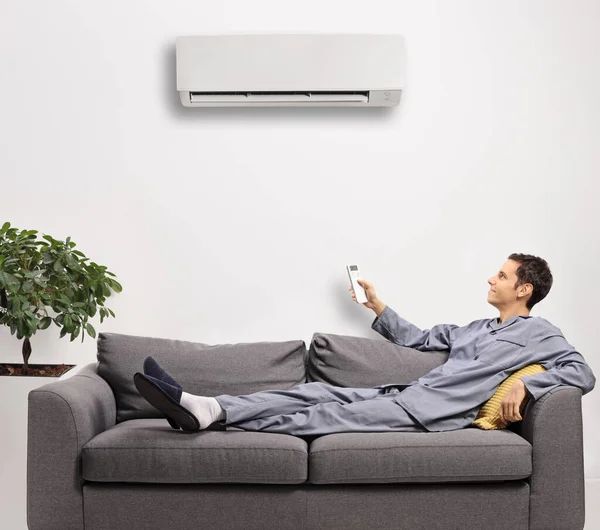 Uzaktan kumandalı pijamalı genç adam evde klima takıyor.