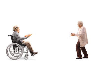 Tekerlekli sandalyedeki yaşlı bir adamın beyaz arka planda izole edilmiş yaşlı bir kadına plastik disk attığı uzun bir profil çekimi.