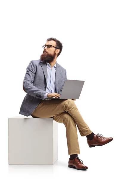 Brodaty Mężczyzna Siedzący Białej Kostce Laptopem Patrzący Siebie Białym Tle — Zdjęcie stockowe
