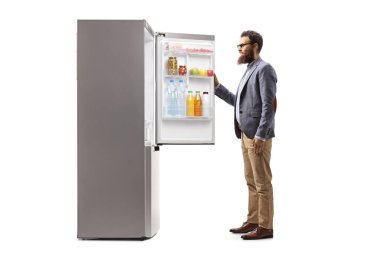 Gözlüklü sakallı adam beyaz arka planda izole edilmiş bir buzdolabını açıyor.