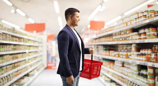 Jovem Supermercado Carregando Uma Cesta Compras Vermelha Olhando Prateleiras — Fotografia de Stock