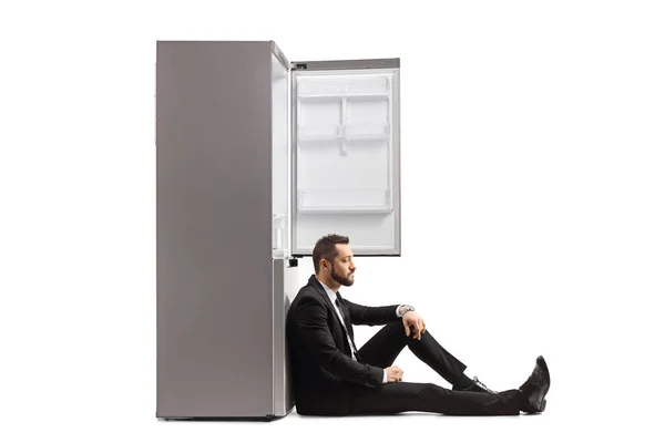 Disappointed Businessman Sitting Floor Leaning Empty Fridge Isolated White Background — Stock Photo, Image