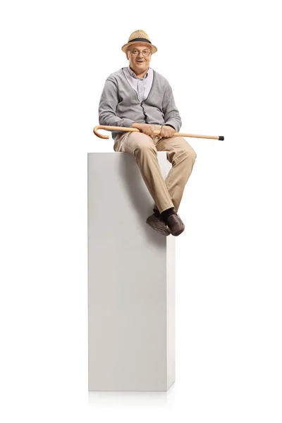 老人坐在一根柱子上 手里拿着一根被白色背景隔离的手杖 — 图库照片