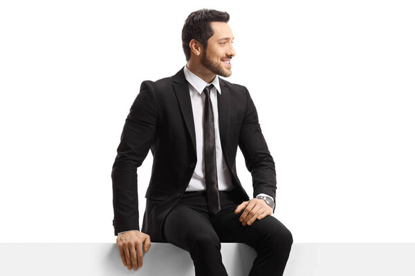 Young handsome man in a suit sitting on a panel isolated on white background