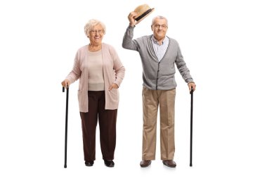 Yaşlı bir beyefendi, beyaz arka planda izole edilmiş yaşlı bir kadınla ayakta ve şapkayla selamlaşıyor.