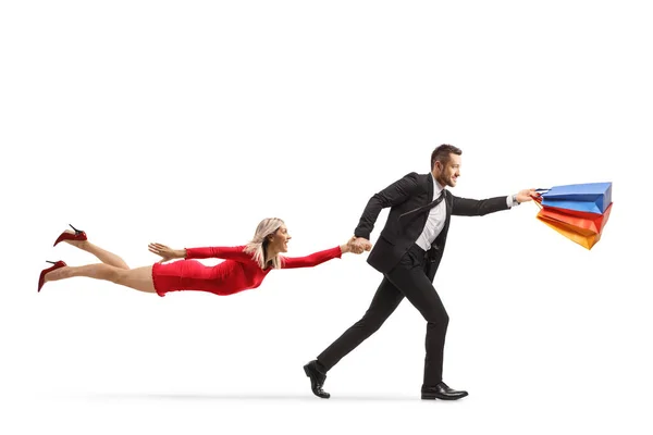 男はショッピングバッグを保持し 白い背景に隔離された赤いドレスで飛んでいる女性と一緒に実行 — ストック写真
