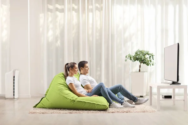 若いです男と女性座っています緑豆バッグArmchairと見ますテレビホーム — ストック写真