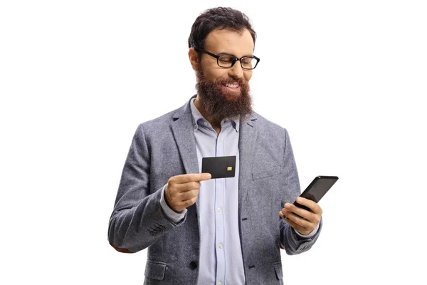 笑顔と白い背景に隔離された携帯電話を見てクレジットカードを持つ髭の男 — ストック写真