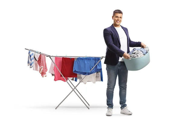 洗濯籠を持って白い背景に隔離されたラックを乾燥服の横に立っている男 — ストック写真