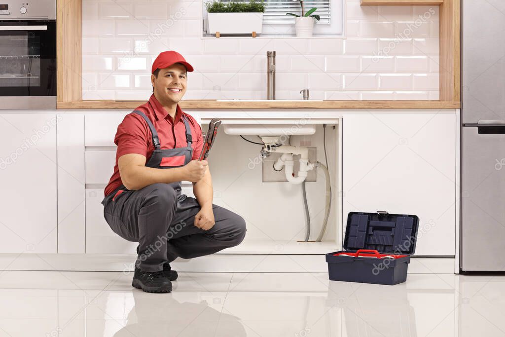 Plumber with a tool box kneeling next to a sink in a modern kitchen