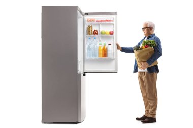 Yetişkin bir adamın market poşeti ile beyaz arka planda izole edilmiş buzdolabını açarken tam boy profil fotoğrafı.