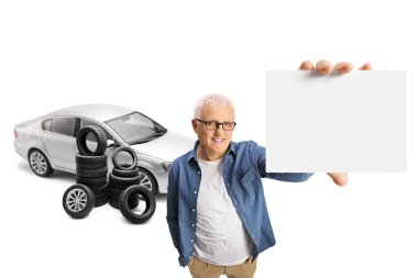 Gümüş renkli arabası ve beyaz arka planda boş bir kart tutan bir yığın lastiği olan olgun bir adam.