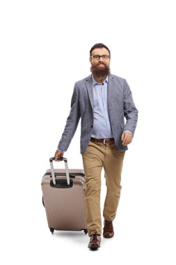 Bavulu çekip beyaz arka planda izole bir şekilde kameraya doğru yürüyen sakallı bir adamın tam boy portresi.