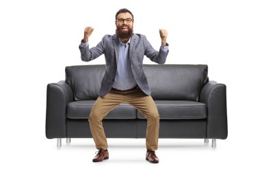 Sakallı adam mutluluğu işaret ediyor ve beyaz arka planda izole bir şekilde kanepenin önüne atlıyor.