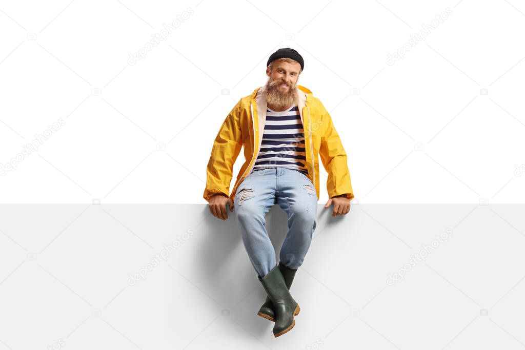 Bearded guy fisherman with a yellow rain coat sitting on a panel isolated on white background