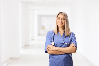 Hastane koridorunda poz veren mavi üniformalı genç bir hemşire.