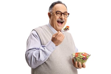 Bir kase salata tutan ve beyaz arka planda bir çatalla yemek yiyen mutlu olgun bir adam.
