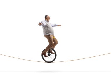 Full length profile shot of a funny mature man riding a mono-cycle on a rope isolated on white background clipart
