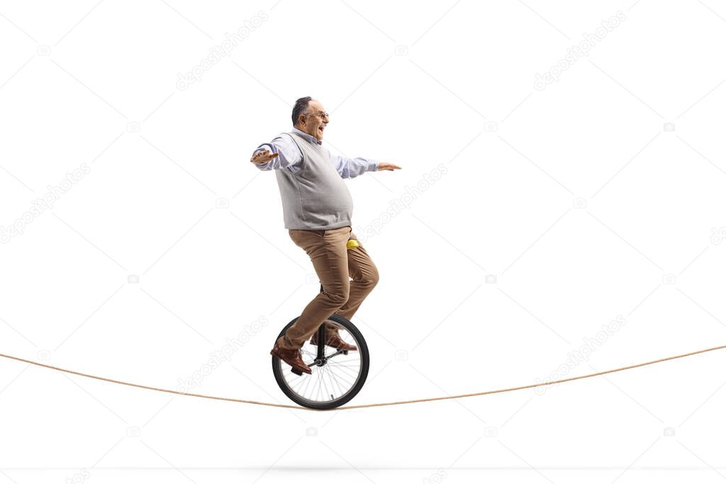 Full length profile shot of a funny mature man riding a mono-cycle on a rope isolated on white background