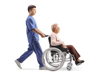 Bir sağlık çalışanının, beyaz arka planda izole edilmiş tekerlekli sandalyedeki yaşlı bir kadın hastayı iterken tam boy profil fotoğrafı.