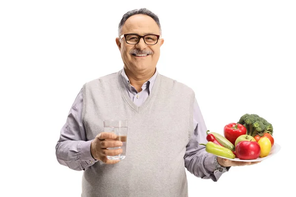 正在微笑的成熟男人 手里拿着一杯水和一个用白色背景隔离的水果和蔬菜制成的盘子 — 图库照片