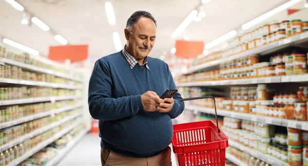 Volwassen Man Met Een Winkelmandje Typen Een Smartphone Een Supermarkt — Stockfoto