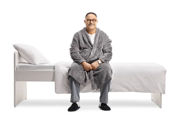 穿着睡衣和长袍的成熟男人坐在床上 与白色背景隔离 — 图库照片