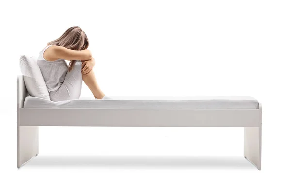 白い背景に隔離されたベッドの上に座っているパジャマの悲しい女性 — ストック写真