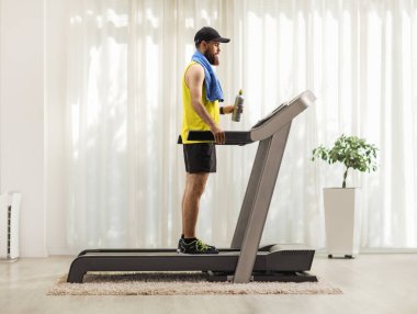 Evdeki koşu bandında duran sakallı bir adamın tam boy fotoğrafı.