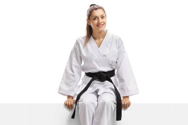 Karate kimonolu ve siyah kuşaklı bir kadın beyaz arka planda izole edilmiş bir pankartta oturuyor.