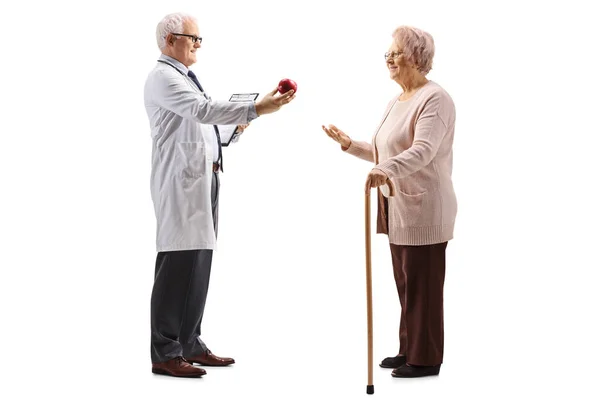 白い背景に孤立した高齢者の女性にリンゴを与える医師の完全な長さのプロフィールショット — ストック写真