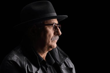 Siyah arka planda şapkası ve deri ceketi olan olgun bir adamın profil fotoğrafını çek. 