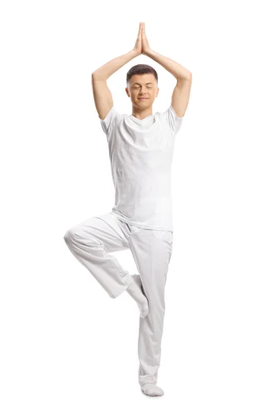 白い服を着た若い男の完全な長さの肖像画ヨガを練習し 白い背景に隔離された1本の足に立つ — ストック写真