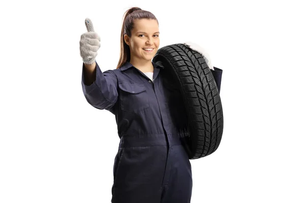 女机修工背着车胎 给一个用白色背景隔开的大拇指标志做手势 — 图库照片