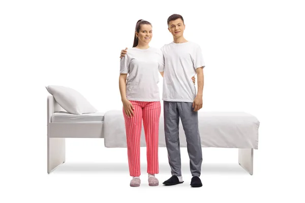 身穿睡衣的男女青年站在被白色背景隔离的床前的全长肖像 — 图库照片