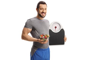 Elinde bir terazi ve beyaz arka planda izole edilmiş bir kase salata tutan genç adam. 