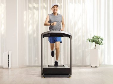 Evdeki koşu bandında koşan yaşlı bir adamın tam boy portresi.