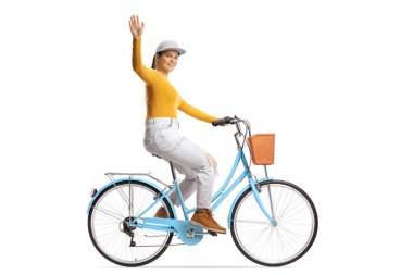 Şehir bisikletine binen ve beyaz arka planda izole edilmiş kameraya el sallayan genç bir kadının tam boy profil çekimi.