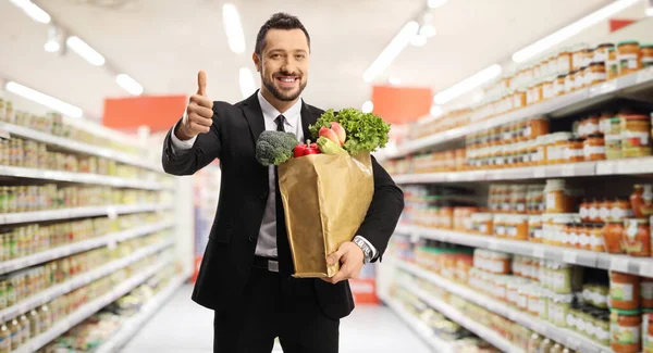 Młody Biznesmen Torbą Zakupy Pozujący Supermarkecie Gestykulujący Znakiem Kciuk Górę — Zdjęcie stockowe