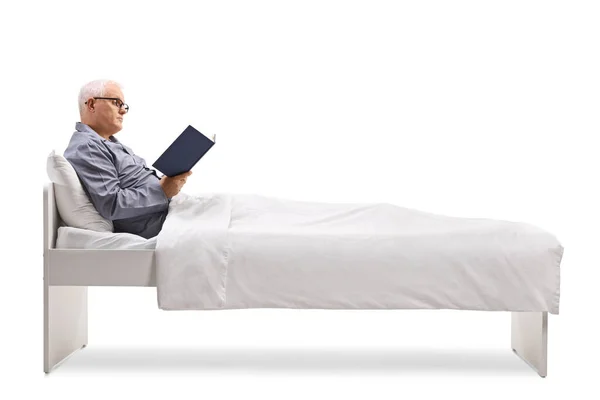 成熟した男でパジャマでベッドの上に座って下さいDuvetと読書A本孤立した上に白い背景 — ストック写真
