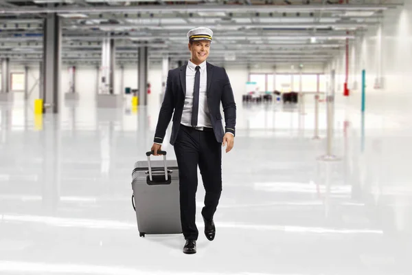 Full length portrait of a pilot walking and pulling at an airport terminal building