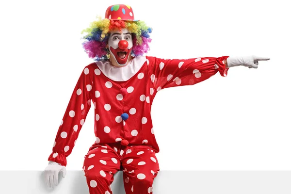 Grappige Clown Zittend Een Wit Paneel Wijzend Naar Zijkant Geïsoleerd — Stockfoto